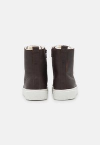 Brown leather ankle boots with a textured finish, white rubber soles, side zippers, and a soft interior lining.