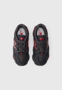 Sapatilhas de malha preta e sintética com detalhes em vermelho, bico arredondado, design com atacadores e sola acolchoada. Logótipo da New Balance visível.