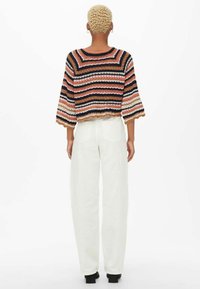 Szydełkowy sweter w wielokolorowe paski, z szerokimi rękawami i skróconym fasonem. Połączony z luźnymi białymi spodniami.
