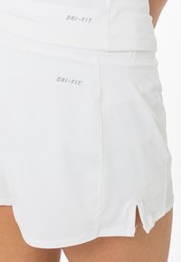 Pantalones cortos blancos DRI-FIT con una textura suave, que cuentan con aberturas laterales para movilidad y una sutil marca reflectante en la cintura y el lateral.