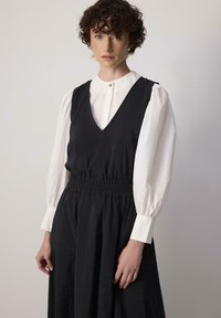 Must must, mille avatud V-kaelusega ja kokkutõmmatava vöökohtadega, millel on peal valge pika varrukaga särk, millel on puhvvarrukad ja nööpidega krae.