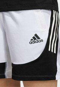 Mustavalkoiset urheilushortsit, joissa on verkkotekstuuri, kolme pystysuoraa raitaa toisella sivulla ja Adidas-logo edessä.