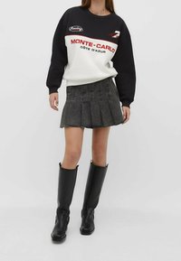 Zwart-witte sweater met de tekst "MONTE-CARLO CÔTE D’AZUR", gecombineerd met een geplooide zwarte spijkerrok en zwarte laarzen tot aan de knieën.