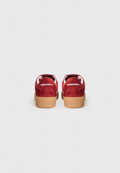 Red suede sneakers with a textured rubber sole, featuring white accents and branding on the back. Rounded heel and lace-up design.