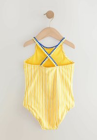 Gelb gestreifter Badeanzug mit Rückendesign in Kreuzform, der blaue Akzente entlang der Träger aufweist. Glatte Stofftextur, hängt an einem Holzkleiderbügel.