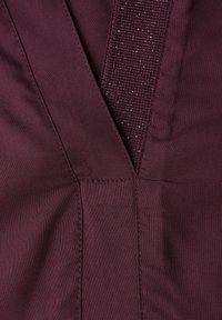 Burgunderrødt stof med en struktureret stribe med subtil glans. Glat, blød tekstur med synlige syningsdetaljer.