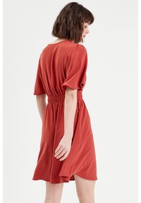 Vestido rojo de manga corta con cintura ajustada, hecho de un tejido liviano. El dobladillo es ligeramente acampanado y presenta un ajuste relajado.