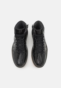 Svarta hög-top sneakers i glänsande lackläder, med perforerade detaljer, platta snören och en gummisula i gumfärg.