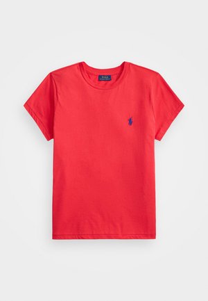 Punane puuvillane lühikeste varrukatega t-särk ümarate kaelustega ja väikese sinise broderitud logoga vasakul rindkeres. Sile tekstuur, lõdva sobivusega.