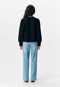 Pull noir avec des manches bouffantes, associé à un jean large bleu clair. Le tissu paraît lisse avec une coupe décontractée et un col rond.
