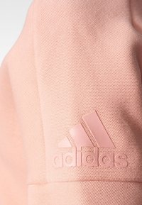 Tela texturizada rosa con un logo de Adidas en relieve que presenta tres rayas y el nombre de la marca en la manga de una prenda.