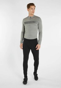 Maglietta da ciclismo grigia a maniche lunghe con dettagli a strisce nere, chiusura frontale a zip, abbinata a leggings neri attillati e scarpe nere.