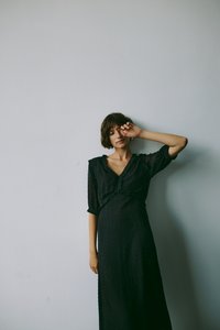 Crna haljina s teksturiranom tkaninom s točkicama, napućenim rukavima i dubokim V-izrezom. Dizajn je dug i lepršav.