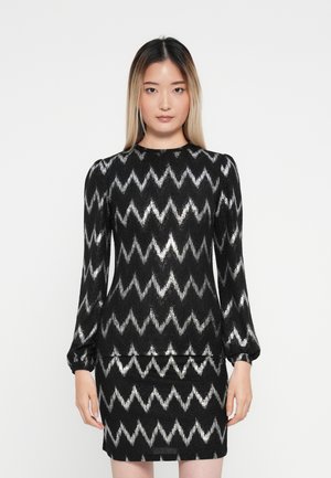 Pull à motif zigzag noir et argent avec des manches longues et un col rond, associé à une jupe assortie. Matériau texturé.