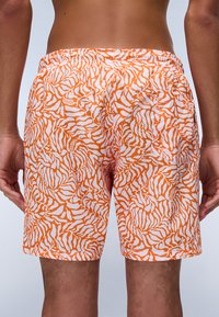 Zwemshorts in oranje en wit met een zebra-streep patroon. Elastische tailleband, lichtgewicht stof en een minimalistisch merkteken.