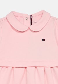 Vestido de algodón rosa con cuello redondeado, falda plisada y un pequeño logo bordado. Cuenta con un cierre a presión en la parte trasera y una textura suave.