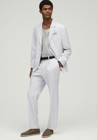 Lys grå dragt med en tætsiddende blazer, matchende bukser og en afslappet grå t-shirt. Accenter inkluderer en blå lommefyr og brune slip-on sko.