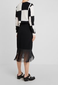 Svetr z vlněné směsi s černobílým kostkovaným vzorem, kombinovaný s černou sukní s třásňovým lemem a klínovými dřeváky.