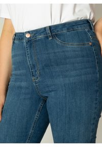 Donkerblauwe denim jeans met een slim fit, voorzien van een knoop- en ritssluiting, riemlussen en voorzakken. Soepele textuur.