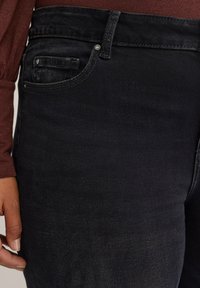Jeans in denim nero con un design a cinque tasche, dettagli di cucitura sottili e una texture morbida, abbinati a una maglietta a maniche lunghe in color bordeaux.