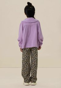 Purple, textured top with ruffled collar paired with loose-fitting, leopard print pants and white sneakers, viewed from the back.