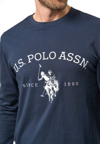 Marineblauw langemouwen T-shirt van katoen. Bevat witte tekst "U.S. POLO ASSN." en een afbeelding van een polo-speler te paard.