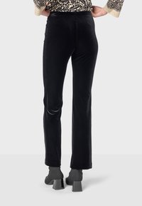 Čierne velúrové nohavice s priliehavým pásom, rozšírenými nohavicami a hladkou textúrou. Nosené s šedými blokovými členkovými čižmami.