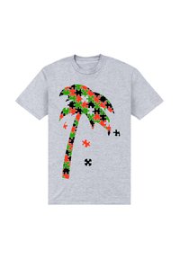 Šedé tričko s designem palmy složeným z puzzle kusů v červené, zelené, černé a oranžové barvě, vedle se nachází několik volných puzzle kusů.