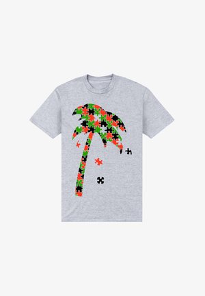Grijze T-shirt met een palmbomen ontwerp, samengesteld uit puzzelstukken in rood, groen, zwart en oranje, met verschillende losse puzzelstukken in de buurt.