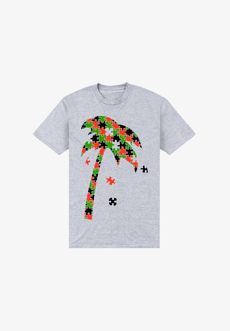 Šedé tričko s designem palmy složeným z puzzle kusů v červené, zelené, černé a oranžové barvě, vedle se nachází několik volných puzzle kusů.
