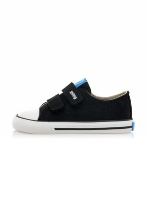 Zapatillas de lona negras con punta de goma blanca, dos correas de velcro ajustables y acentos azules en la lengüeta y el talón. Suela a rayas en blanco y negro.