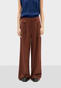 Pantaloni a gamba larga marroni con vita alta, realizzati in tessuto morbido; presentano un bottone anteriore, pieghe e tasche. Abbinati a un top in maglia blu navy.