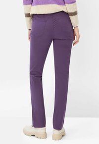 Paarse recht gesneden broek van zachte stof, met achterzakken en zoomdetails. Gecombineerd met lichtgekleurde schoenen met een dikke zool.