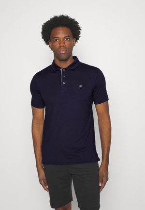 Navy polo shirt made of cotton blend with short sleeves, three-button placket, and a small white logo on the left chest.