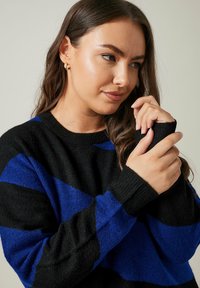 Pull rayé noir et bleu avec un col rond et des manches longues à poignets côtelés. Texture douce, gros plan sur des mains.