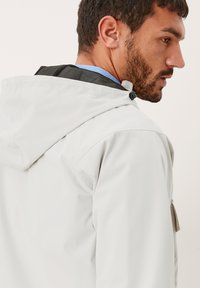 Hellgraue wasserdichte Jacke mit Kapuze, ausgestattet mit einem Netzfutter am Hals und Reißverschluss Taschen. Glatte Textur und minimalistisches Design.