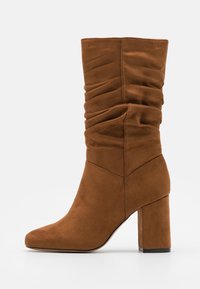 Stivaletto in suede marrone con superiore arricciato, punta affusolata e tacco chunky. La texture liscia e i dettagli delle cuciture mettono in risalto il design.