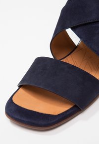 Sandale en daim bleu marine avec larges brides et semelle intérieure en cuir marron clair vue de face sur fond blanc.
