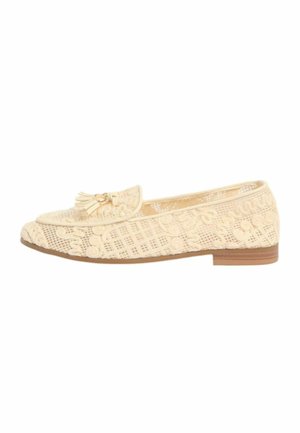 Mocasini beige, cu talpă plată, model floral dantelat, detalii cu ciucuri în partea de sus și talpă maro, văzuți din lateral pe un fundal alb.