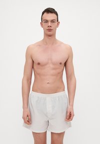 Shorts légers de couleur crème avec une taille élastique et un bouton devant. Texture lisse, design jusqu'aux genoux.