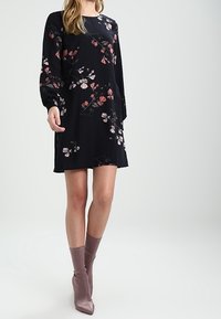 Vestido negro de flores con mangas largas, que presenta patrones de flores en rosa y blanco. Tela suave, forma en A, combinado con botas de tobillo rosa claro.