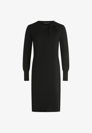 Czarna dzianinowa sukienka z długimi rękawami, okrągłym dekoltem i detalem w postaci kokardy na lewym ramieniu. Gładka tekstura, długość do kolan.