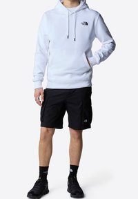 Felpa bianca con cappuccio e tasca a marsupio, con logo nero sul petto, abbinata a pantaloni cargo neri e scarpe nere. Design semplice e funzionale.