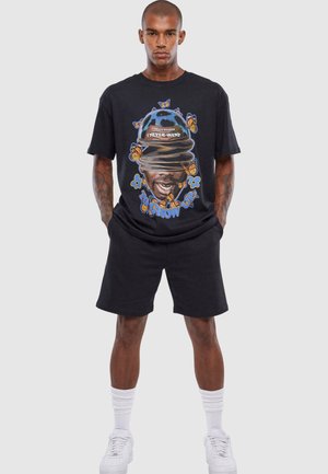 Svart grafisk t-skjorte med et fargerikt design med sommerfugler og tekst. Kombinert med sorte shorts og hvite sneakers. Enkel tekstur.
