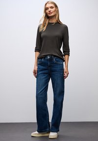 Donkergrijze lange mouwen top gecombineerd met blauwe wijde jeans. De outfit heeft een klassiek ontwerp, een zachte textuur en standaard denimstiksels.