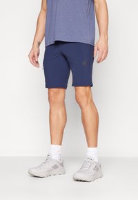Mornarsko športno krilo s slim fit krojem, z zadrgo in detajlom logotipa, v kombinaciji s svetlo sivimi čevlji in belimi nogavicami.