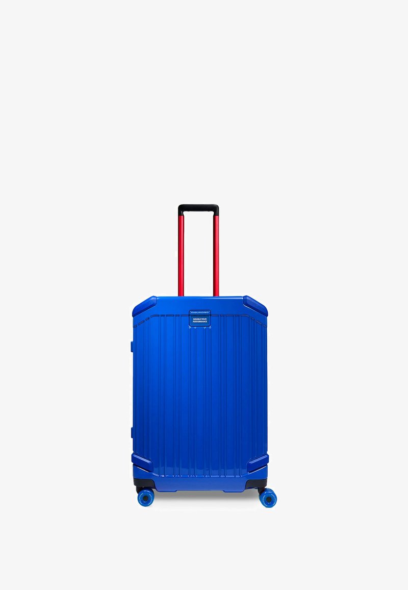 Valigia rigida di colore blu vivace, con scanalature verticali, manico telescopico nero e rosso, e quattro ruote blu per la mobilità.