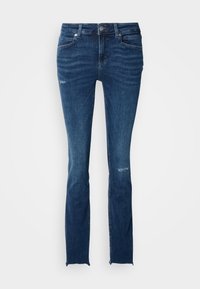 Jean skinny bleu foncé avec légère usure sur la cuisse et le genou, style cinq poches et ourlets bruts.