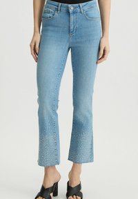 Jeans flared in denim azzurro chiaro con orlo sfilacciato, decorati con piccole pietre lucide trasparenti sul fondo, dotati di cinque tasche e chiusura con bottone frontale.