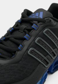 Black athletic shoe with mesh upper, blue accents, and three grey synthetic stripes. Features padded tongue and textured laces.